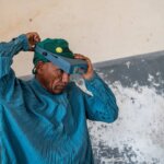 Auf dem Bild ist ein Mann in blauer Operationskleidung zu sehen. Er trägt einen dunkelgrünen Kopfschutz und setzt sich gerade sein Stirngerät auf, um einen Eingriff durchzuführen.